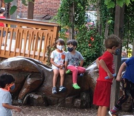 Two young children, masked, converse quietly in a playground.